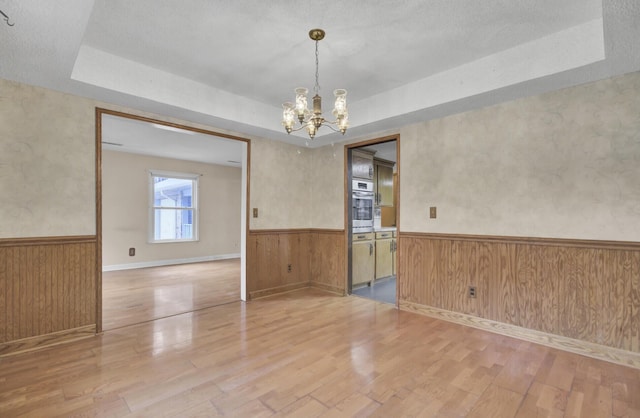 spare room with a raised ceiling, a chandelier, wood-type flooring, and wood walls