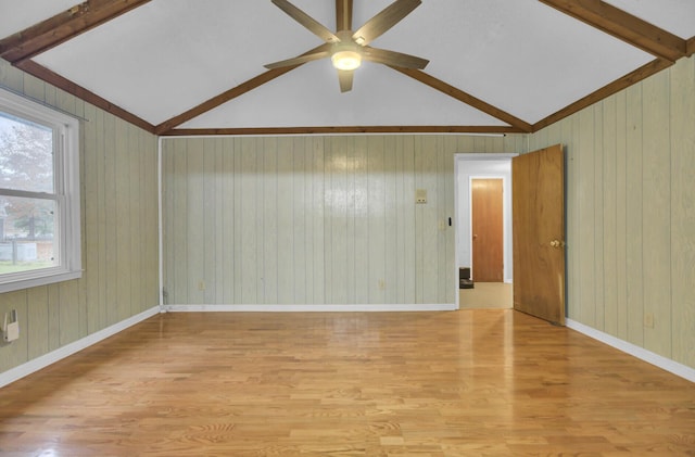 empty room with light wood-type flooring, lofted ceiling with beams, and wood walls