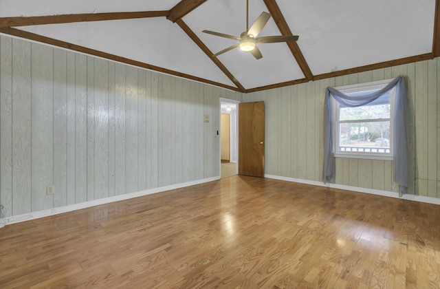 empty room featuring beam ceiling, ceiling fan, wooden walls, and light hardwood / wood-style floors