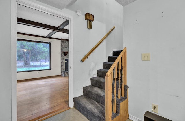 stairway with beam ceiling, wood-type flooring, a textured ceiling, and a brick fireplace