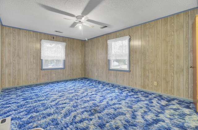 carpeted spare room with ceiling fan, wood walls, and a textured ceiling