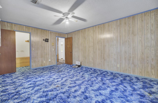 carpeted empty room with a textured ceiling, ceiling fan, and wood walls