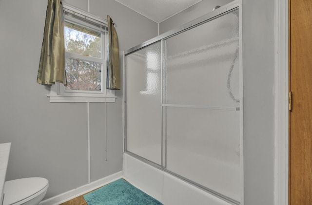 bathroom featuring toilet and bath / shower combo with glass door