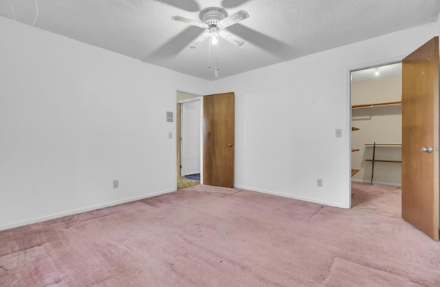 unfurnished bedroom featuring light carpet, a textured ceiling, ceiling fan, a spacious closet, and a closet