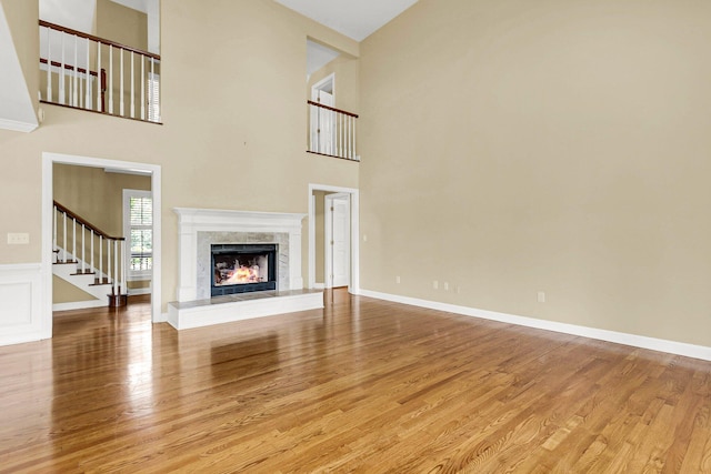 unfurnished living room with light hardwood / wood-style floors, a towering ceiling, and a tiled fireplace