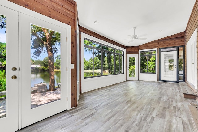 unfurnished sunroom featuring ceiling fan, lofted ceiling, a healthy amount of sunlight, and a water view