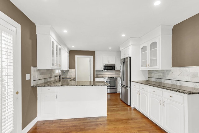 kitchen featuring appliances with stainless steel finishes, backsplash, light hardwood / wood-style floors, sink, and dark stone counters