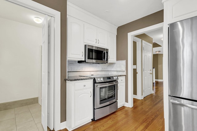 kitchen with stainless steel appliances, light hardwood / wood-style floors, decorative backsplash, white cabinets, and dark stone counters