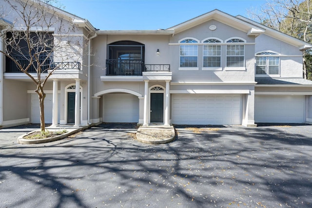 view of front of house featuring stucco siding, a balcony, an attached garage, and driveway