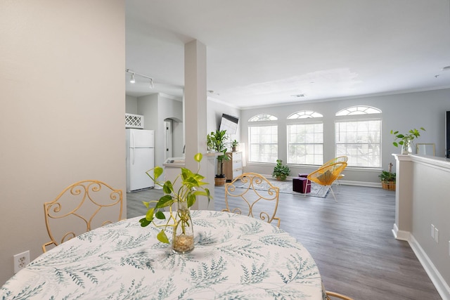 dining room with track lighting, wood finished floors, baseboards, and ornamental molding