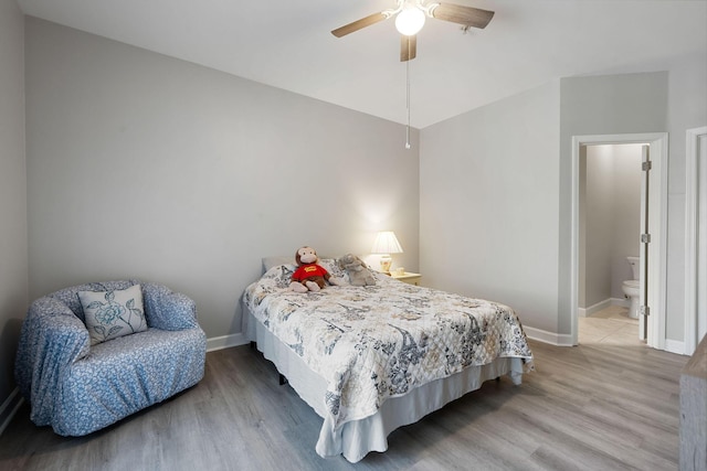 bedroom featuring ensuite bathroom, baseboards, wood finished floors, and a ceiling fan