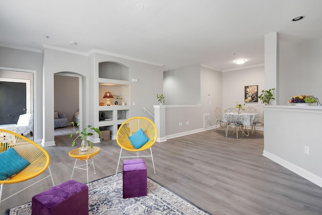 living room featuring built in shelves, wood finished floors, visible vents, arched walkways, and crown molding