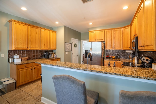 kitchen with backsplash, kitchen peninsula, stone counters, and appliances with stainless steel finishes