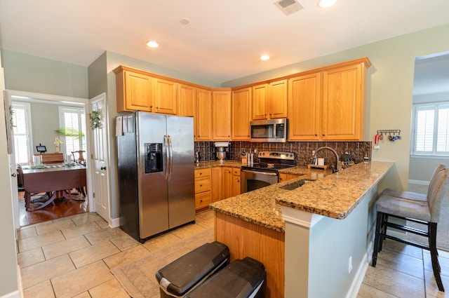 kitchen with a kitchen bar, sink, light stone counters, kitchen peninsula, and stainless steel appliances