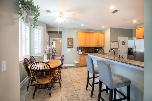 kitchen featuring light brown cabinetry, stainless steel fridge, backsplash, ceiling fan, and light stone counters