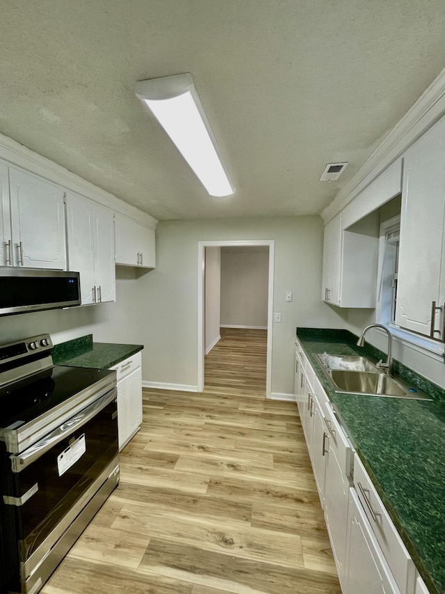 kitchen featuring light wood-type flooring, a textured ceiling, stainless steel appliances, sink, and white cabinets