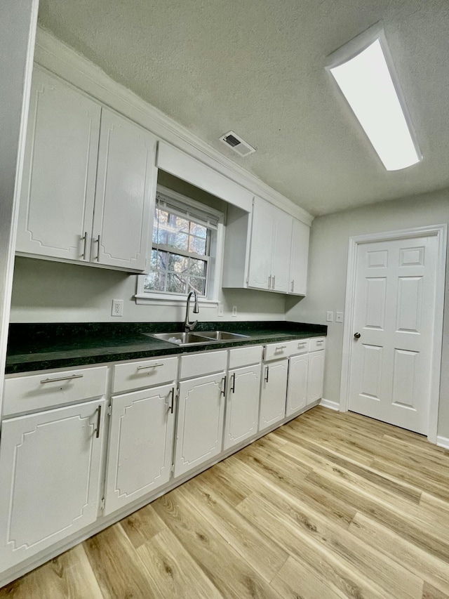 kitchen with white cabinets, light wood-type flooring, sink, and a textured ceiling