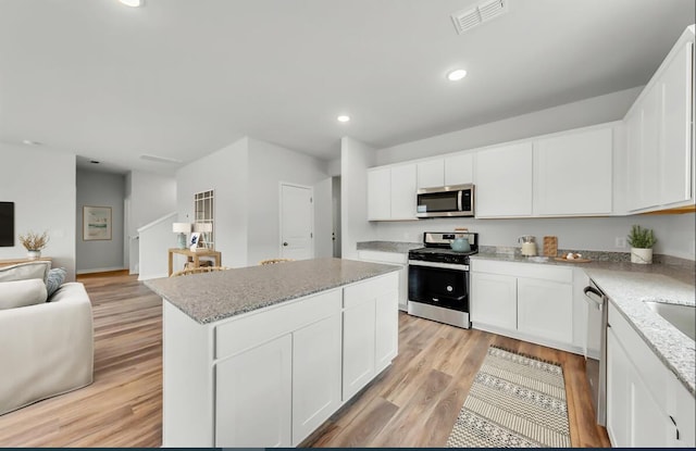 kitchen with appliances with stainless steel finishes, white cabinets, a center island, light stone countertops, and light hardwood / wood-style flooring