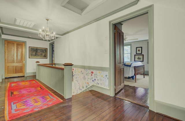 hall with wood-type flooring, ornamental molding, and a chandelier