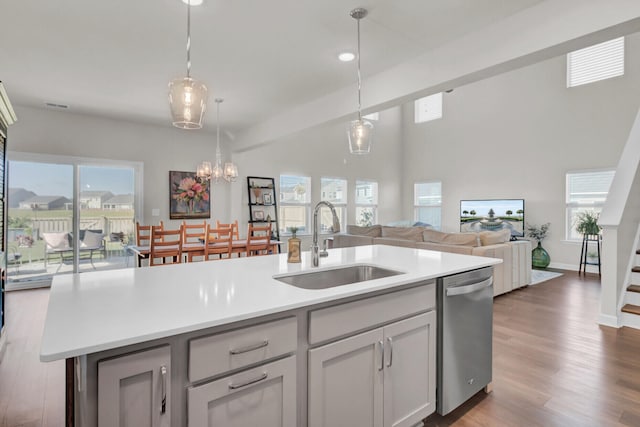 kitchen featuring hanging light fixtures, dishwasher, dark wood-type flooring, sink, and a kitchen island with sink