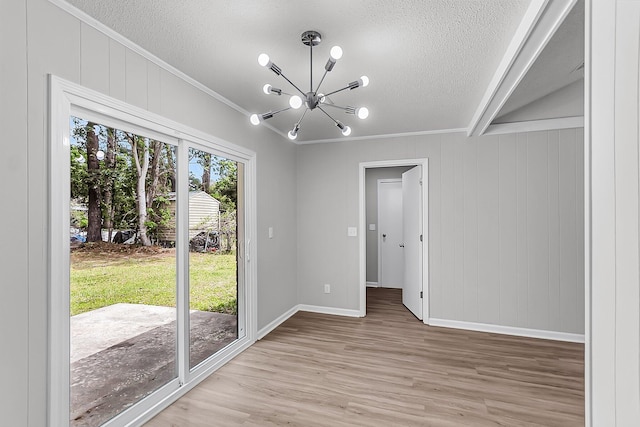 unfurnished room with light wood finished floors, ornamental molding, baseboards, a chandelier, and a textured ceiling