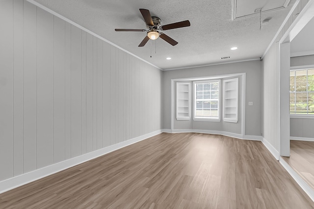 spare room with attic access, wood finished floors, crown molding, and a ceiling fan