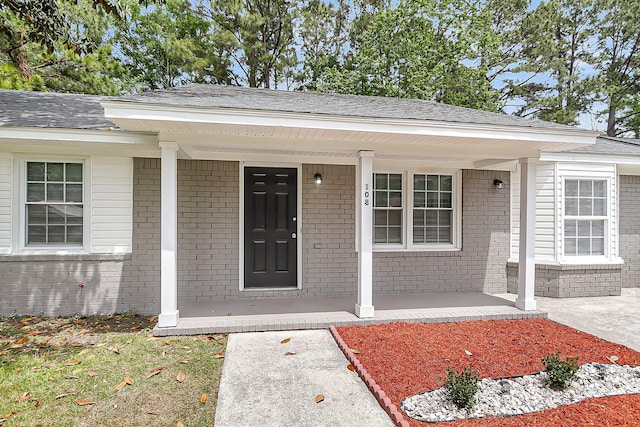 doorway to property featuring a porch and brick siding