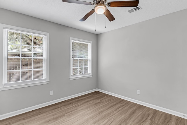 unfurnished room with baseboards, wood finished floors, visible vents, and plenty of natural light