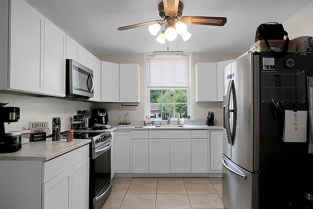 kitchen with appliances with stainless steel finishes, ceiling fan, white cabinetry, sink, and light tile floors