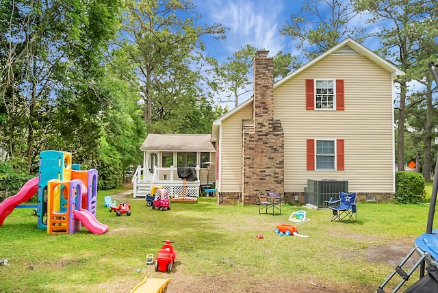 rear view of property featuring central AC unit, a yard, a playground, and a sunroom