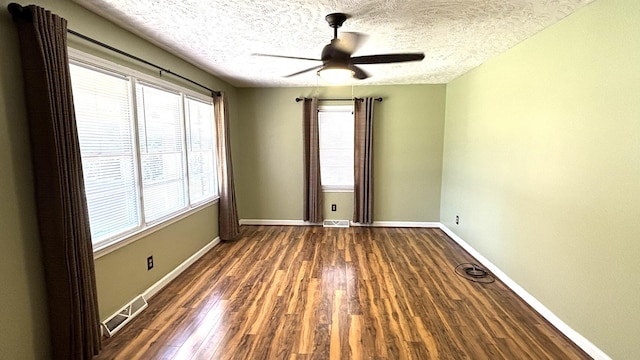 spare room featuring dark wood-style flooring, a ceiling fan, visible vents, baseboards, and a textured ceiling