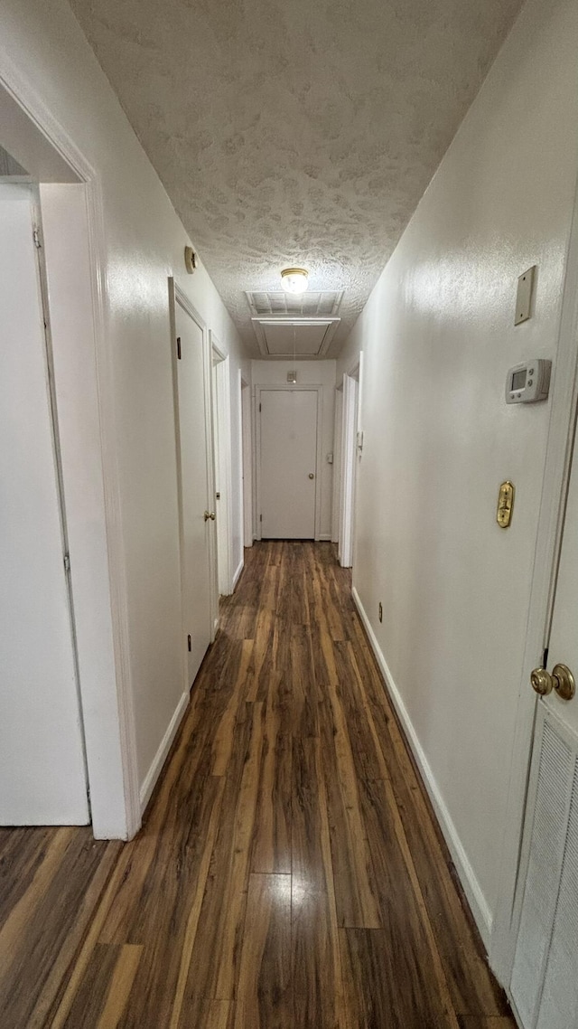 hall featuring baseboards, attic access, a textured ceiling, and dark wood-style flooring
