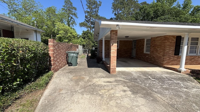 view of property exterior with fence, concrete driveway, an attached carport, and brick siding