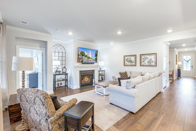 living area featuring visible vents, baseboards, a fireplace with flush hearth, ornamental molding, and wood finished floors