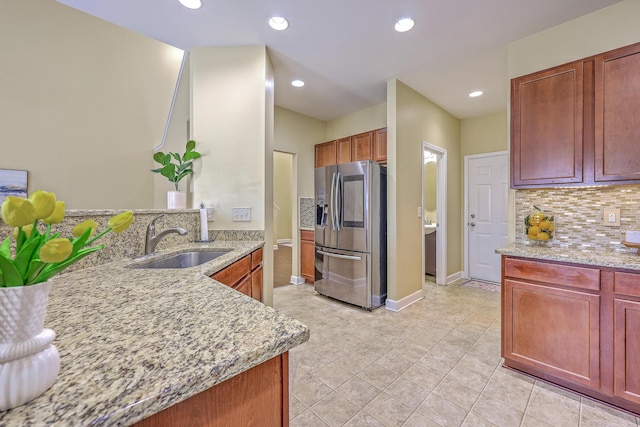 kitchen with recessed lighting, light stone counters, a sink, stainless steel fridge, and backsplash