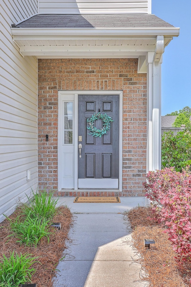 doorway to property featuring brick siding and a shingled roof