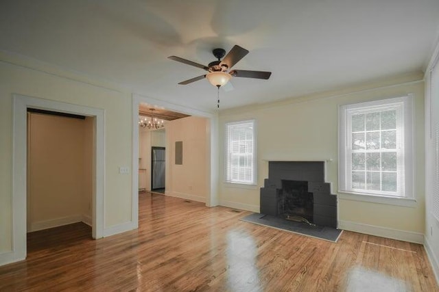 unfurnished living room with hardwood / wood-style flooring, ceiling fan with notable chandelier, crown molding, and a healthy amount of sunlight