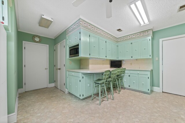 kitchen featuring crown molding, a kitchen breakfast bar, stainless steel microwave, green cabinetry, and a textured ceiling