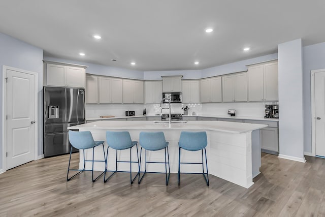 kitchen featuring stainless steel appliances, a kitchen breakfast bar, light wood-style floors, and an island with sink