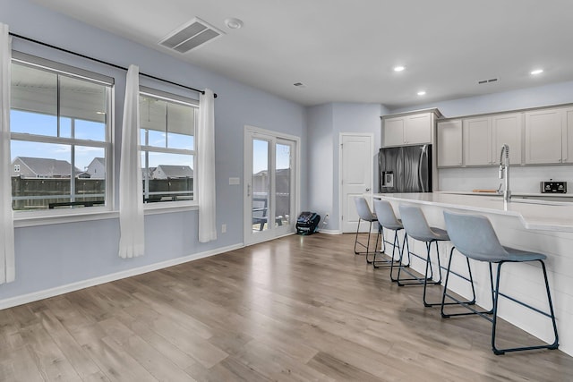 kitchen with visible vents, light wood finished floors, a breakfast bar, stainless steel fridge with ice dispenser, and light countertops