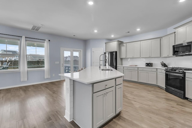 kitchen with visible vents, decorative backsplash, appliances with stainless steel finishes, light wood-style floors, and a sink