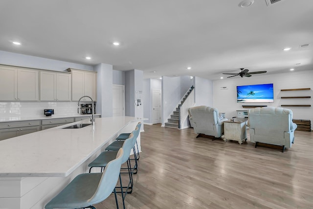 kitchen with tasteful backsplash, open floor plan, light wood-style flooring, a kitchen breakfast bar, and a sink