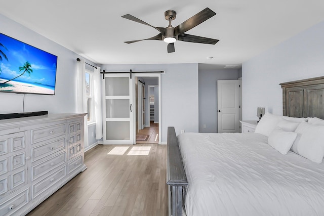 unfurnished bedroom featuring ceiling fan, a barn door, baseboards, and wood finished floors