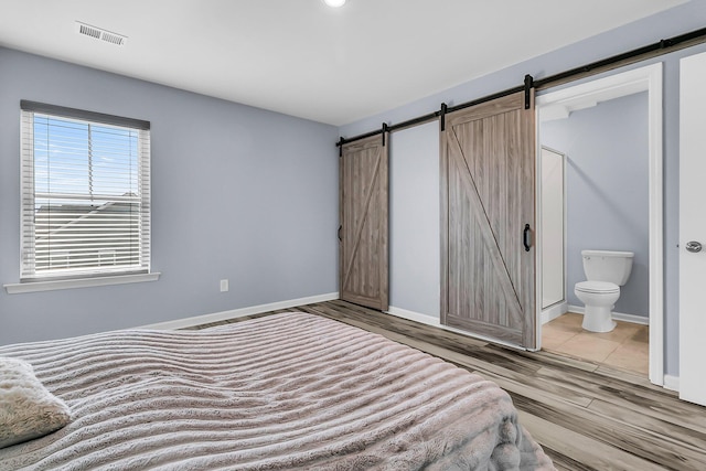 bedroom featuring visible vents, light wood-style flooring, ensuite bath, and a barn door