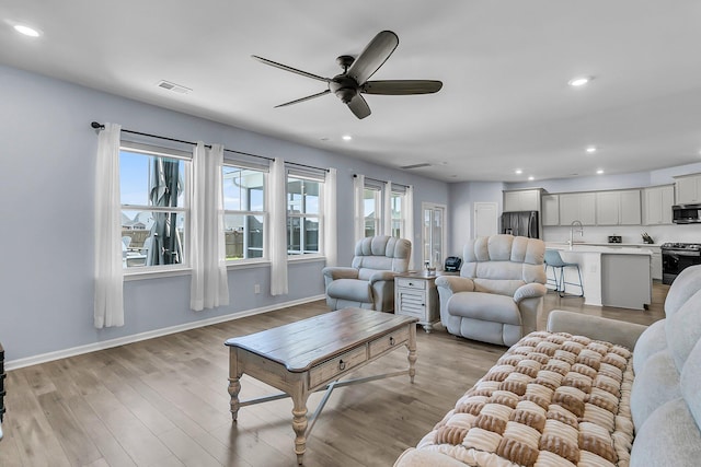 living area with recessed lighting, visible vents, light wood-type flooring, and baseboards