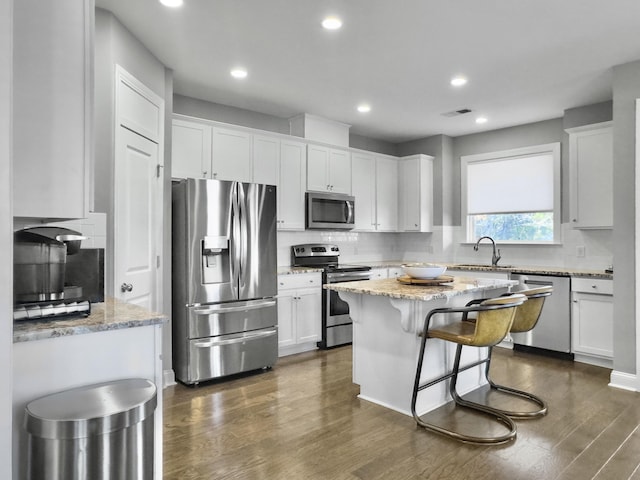 kitchen with stainless steel appliances, light stone countertops, a kitchen island, and white cabinets