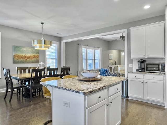 kitchen with dark wood-type flooring, white cabinetry, light stone counters, a kitchen island, and pendant lighting