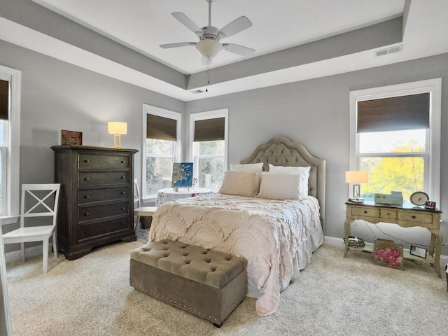 bedroom with a raised ceiling, light carpet, and ceiling fan