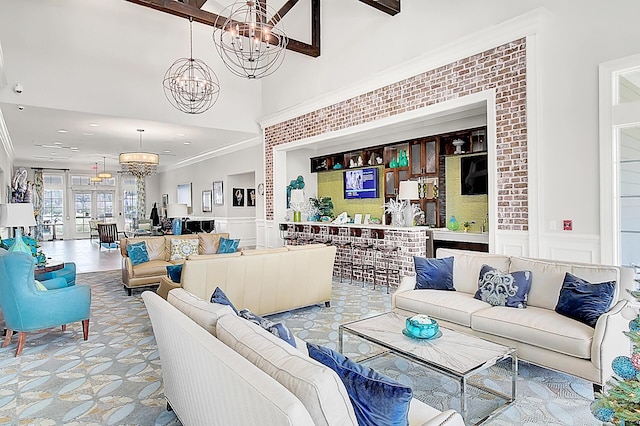 living room with an inviting chandelier, a towering ceiling, ornamental molding, and french doors