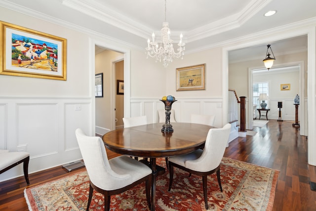 dining space featuring dark wood-type flooring, crown molding, an inviting chandelier, and a tray ceiling